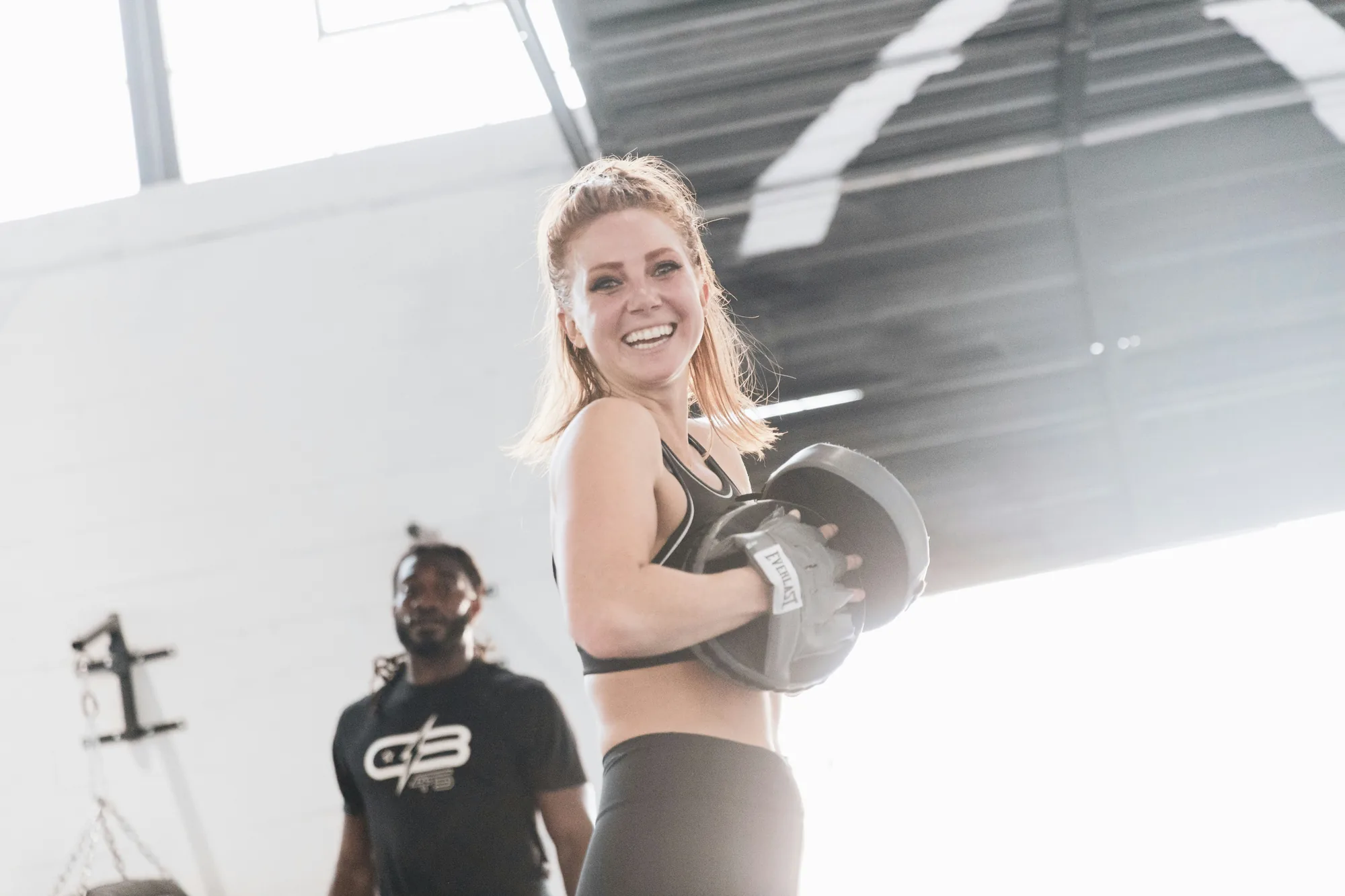 Smiling woman holding a weight plate in a bright gym