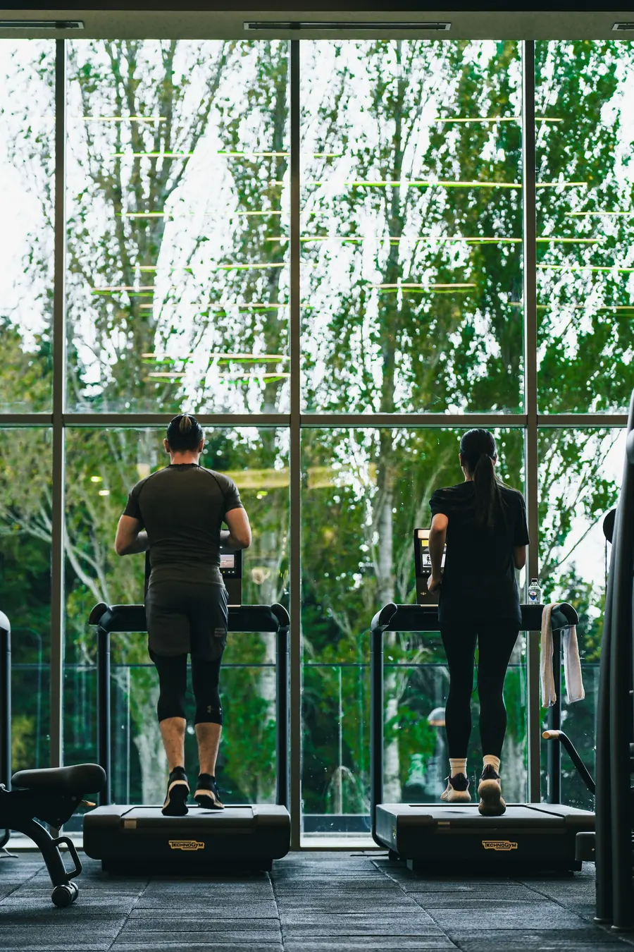 Two people running on treadmills by a big window